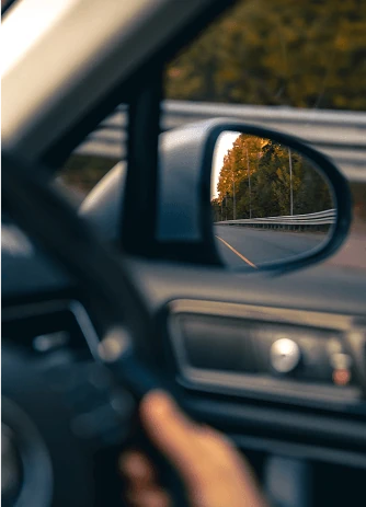 A driver’s hand on the steering wheel, with the road reflected in the wing mirror
